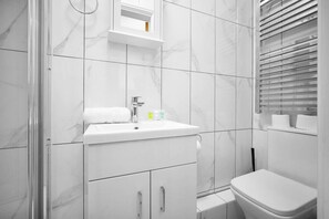 Un baño con lavamanos, inodoro y zona de ducha blancos.