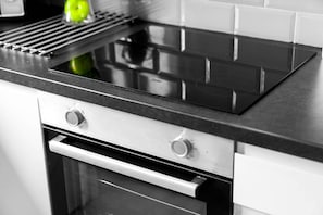 A kitchen with a black induction cooktop, a stainless steel oven, and a white tiled backsplash.