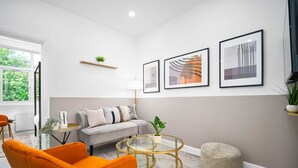 Un salon moderne avec un canapé, des fauteuils orange, une table basse ronde en verre et des œuvres d’art encadrées accrochées au mur.
