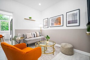 A modern living room with a sofa, orange chairs, a round glass coffee table, and framed artwork on the wall. - Luxury Apartment  - WiFi (Birmingham)