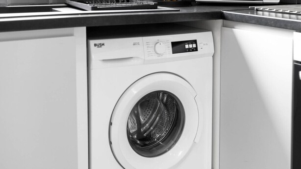 Un lave-linge à chargement frontal dans une cuisine moderne, avec un plan de travail et des meubles de rangement.