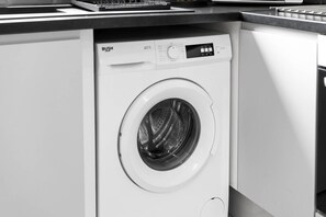 A front-loading washing machine in a modern kitchen with a countertop and cabinetry.