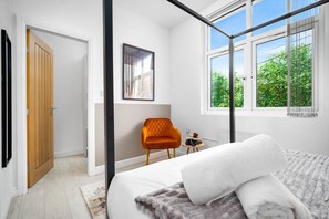 Un dormitorio con cama, ventana con vista a la vegetación, puerta y una silla.