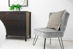 Une chambre moderne avec un fauteuil gris, une commode en bois foncé et un coussin à motifs.