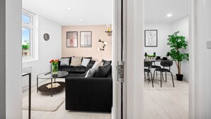 En moderne stue med en sort sofa, et glasbord og et spiseområde med bord og stole.
