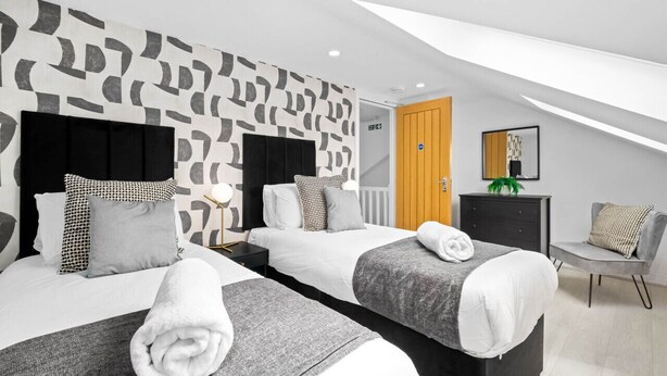 Et moderne hotelværelse med to senge, en trædør, et lille skrivebord og en stol.