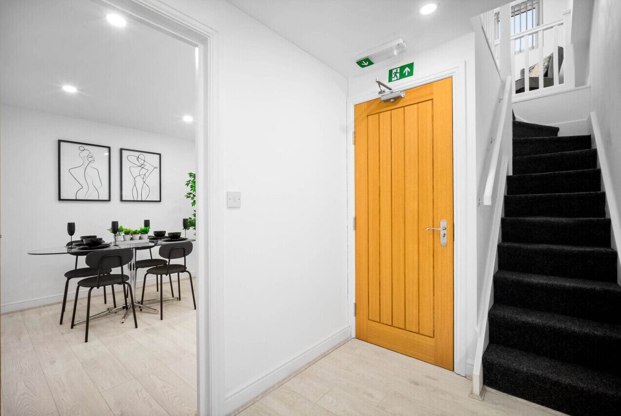 A modern interior with a wooden door, a staircase, and a dining area with black chairs and a table.