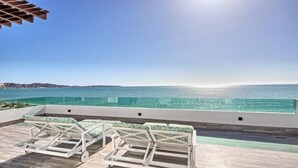 Une terrasse sur le toit, dotée de deux chaises longues et d’une balustrade en verre, offrant une vue imprenable sur une mer d’un bleu profond.