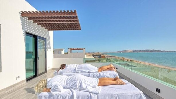 Un balcon avec deux lits, une pergola et une vue sur la mer.