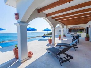 A covered outdoor area with a pool, lounge chairs, and umbrellas overlooking the sea. - Roca Chaac Owner Suite (Isla Mujeres)