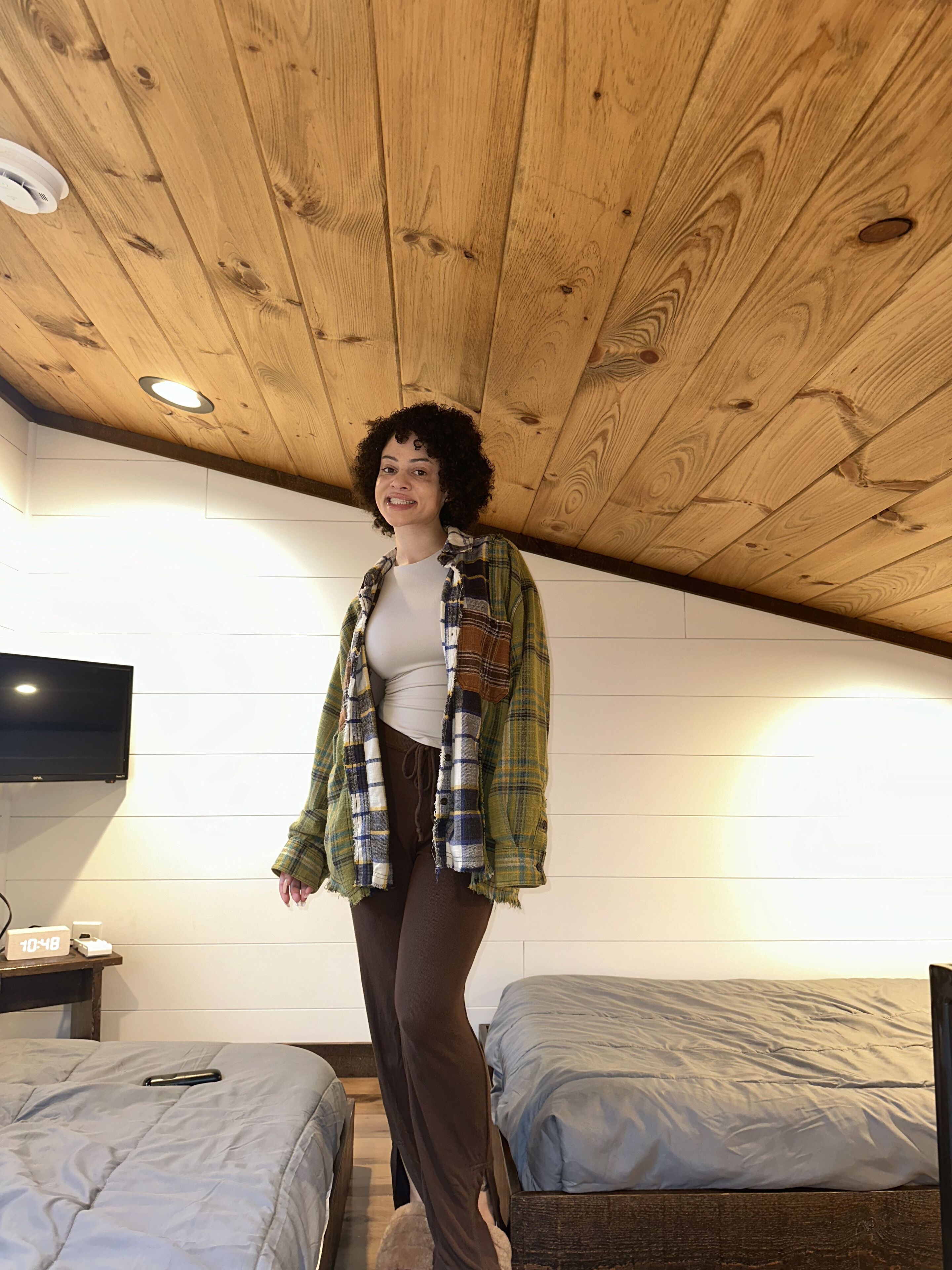 A room with wooden ceiling, two beds, a TV, and a clock.