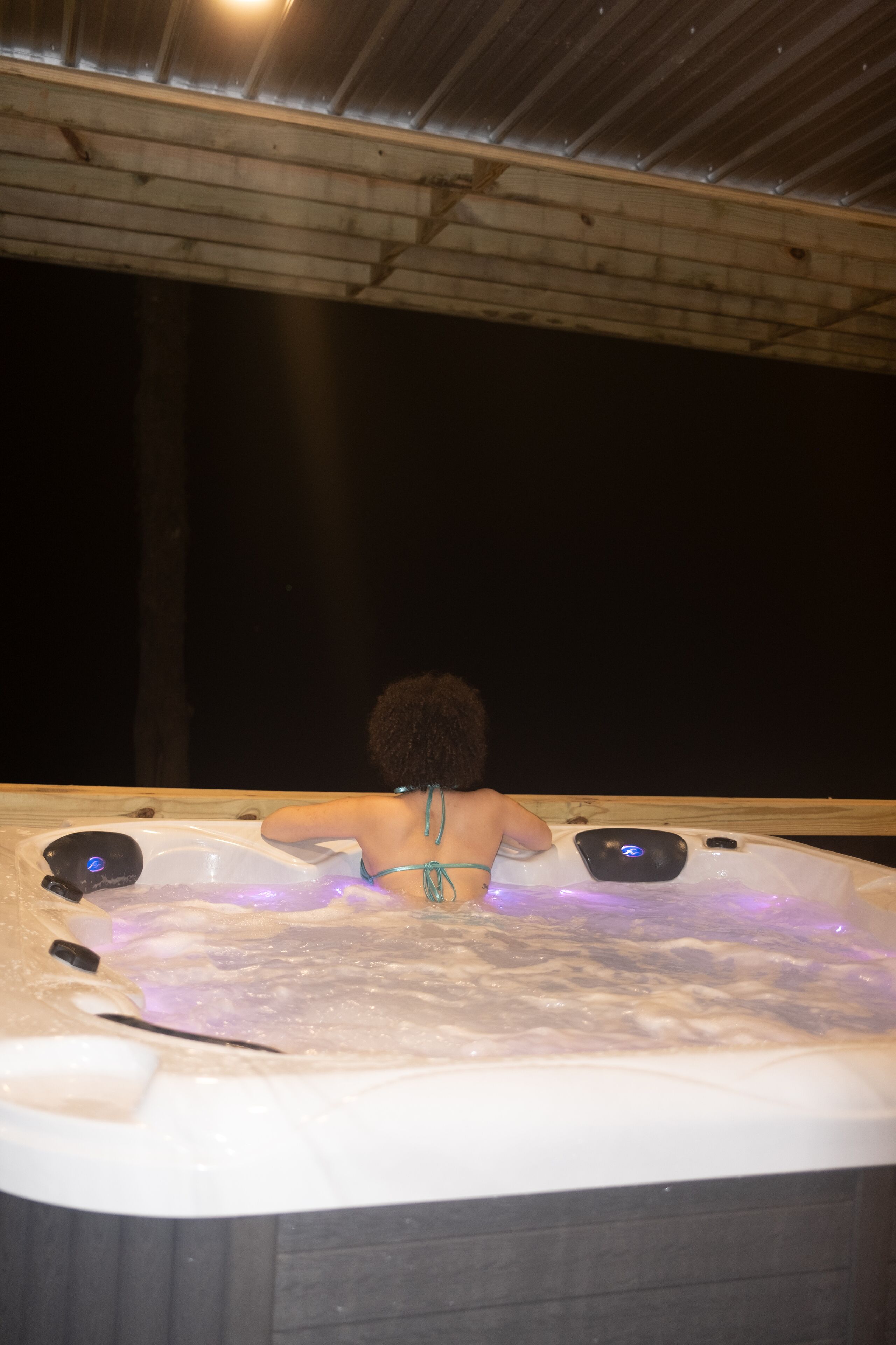 Une personne dans un bain à remous, avec un plafond en bois et un arrière-plan sombre.