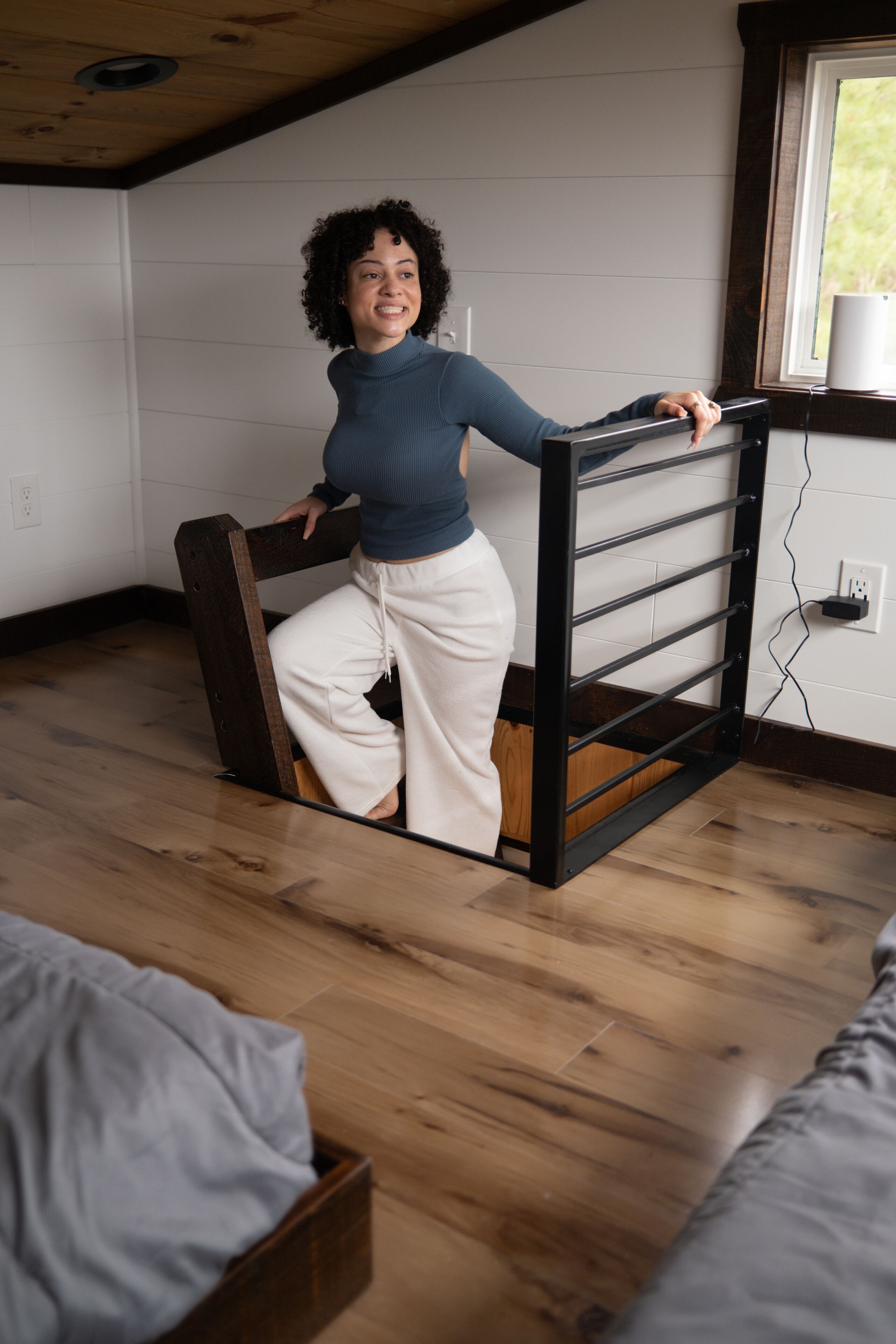A person in a room with wooden floors, a bed, a window, and a white wall.