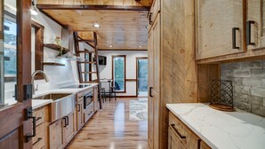 A modern kitchen with wooden cabinetry, a marble countertop, and a view to the outside. - Cozy Couples Treehouse w Hot Tub, Fire Pit, Pet Friendly, Lake Access (Morganton)