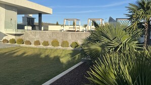 A modern building with a covered outdoor area, a well-maintained lawn, and a variety of plants. - Villalemar Alojamiento Rural 5 Estrellas (Urda)
