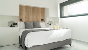A modern bedroom with a wooden headboard, a bed with grey bedding, bedside tables with lamps, and a window providing natural light. - Villalemar Alojamiento Rural 5 Estrellas (Urda)