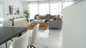 A modern living room with a grey sofa, a coffee table, and a dining area with a table and chairs. - Villalemar Alojamiento Rural 5 Estrellas (Urda)