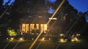Una casa con porche techado, mobiliario exterior y jardín iluminado.