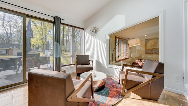 Una sala de estar moderna con un gran ventanal que da a un patio exterior, una mesa de centro redonda y muebles contemporáneos.