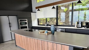 Une cuisine moderne dotée d’un îlot central, d’appareils électroménagers en acier inoxydable et de grandes fenêtres.