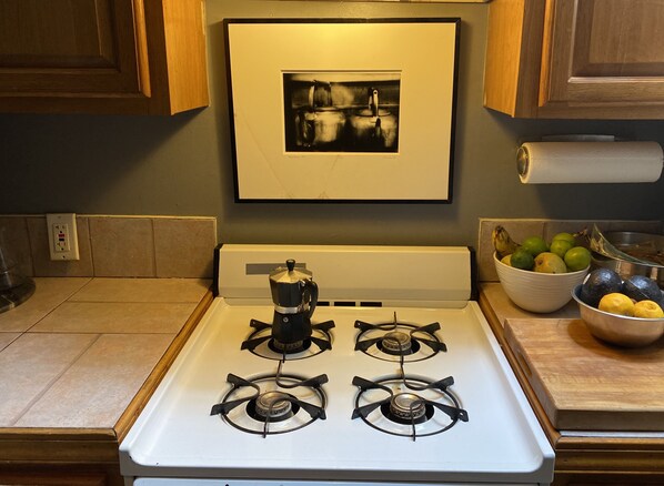 Una cocina con estufa, cafetera y un cuadro en la pared.