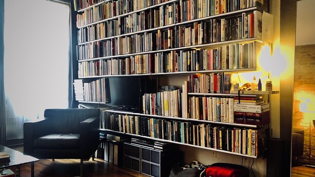 Un salon chaleureux avec une grande bibliothèque remplie de livres, un fauteuil confortable et un téléviseur.
