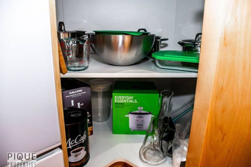 Ein Küchenregal mit einer Edelstahl-Schüssel, einem grünen Topf, einem McCafé-Kaffeebehälter und einer Kiste mit der Aufschrift 'Everyday Essentials'.