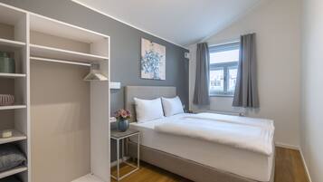 Ein Schlafzimmer mit einem Bett, einem Nachttisch mit einer Vase, einem Kleiderschrank und einem Fenster mit Vorhängen.