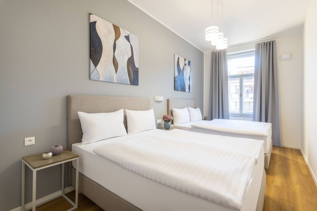 Habitación de hotel con dos camas, una mesita y obras de arte en las paredes.