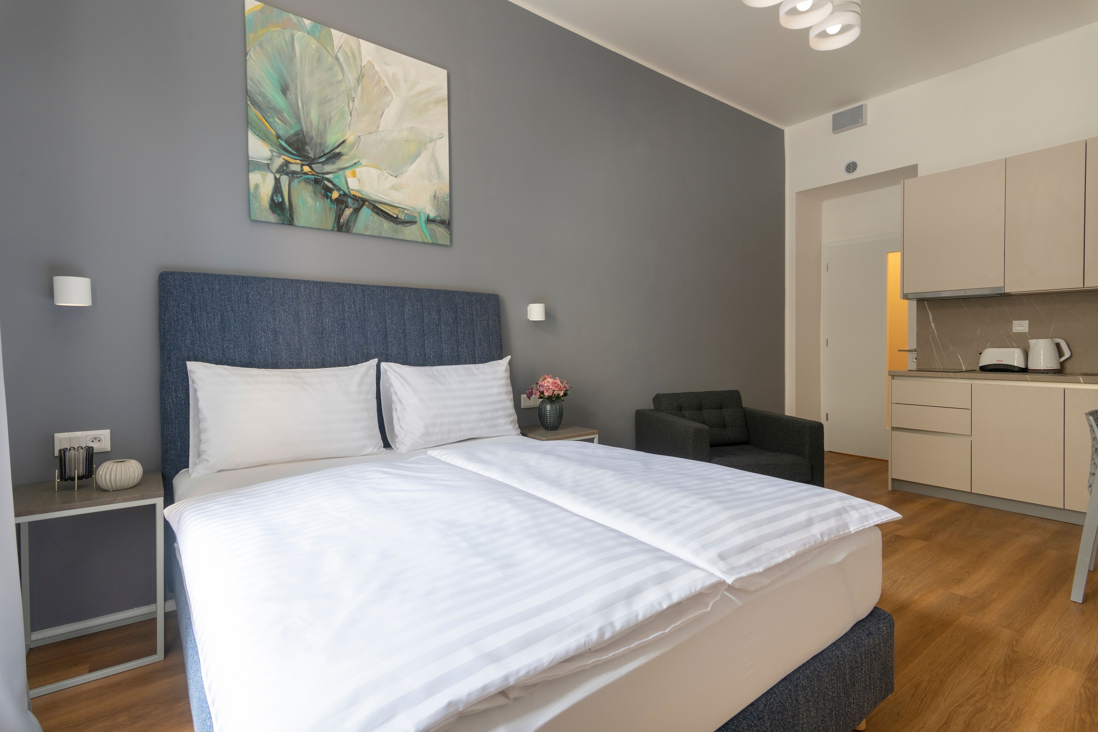 Una habitación de hotel moderna con una cama grande, un escritorio pequeño, una silla y una kitchenette.