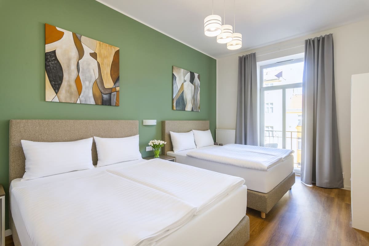 Habitación de hotel con dos camas, paredes verdes, arte abstracto, una ventana con cortinas y vistas al exterior.