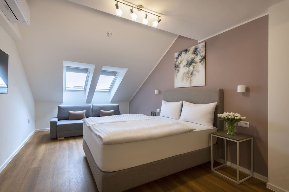 Un dormitorio moderno con una cama grande, un sofá, una mesita con flores y un tragaluz.