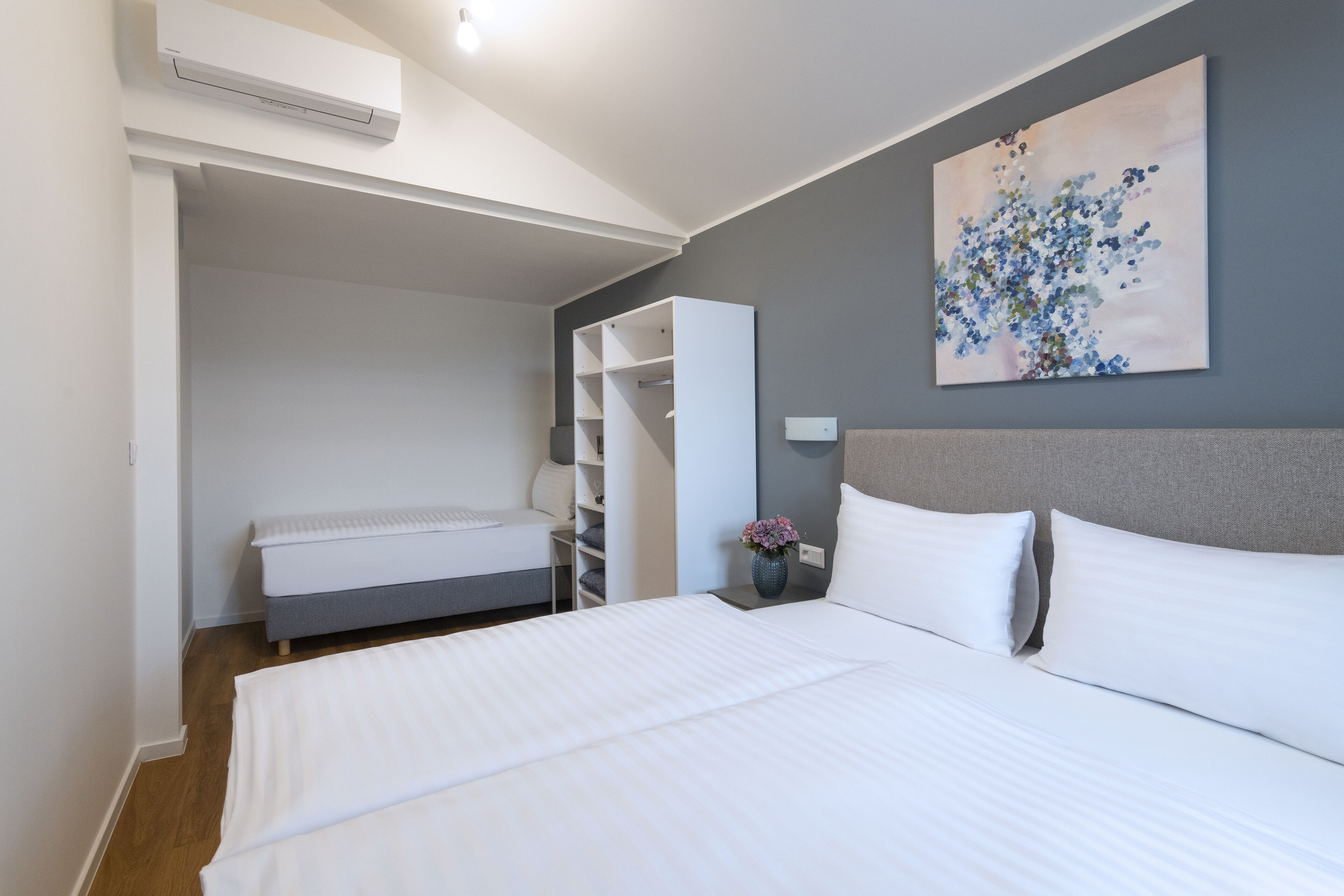 A modern bedroom with a large bed, a walk-in closet, and a painting on the wall.