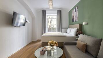 Ett modernt hotellrum med en säng, en soffa, en tv och ett runt bord med blommor.