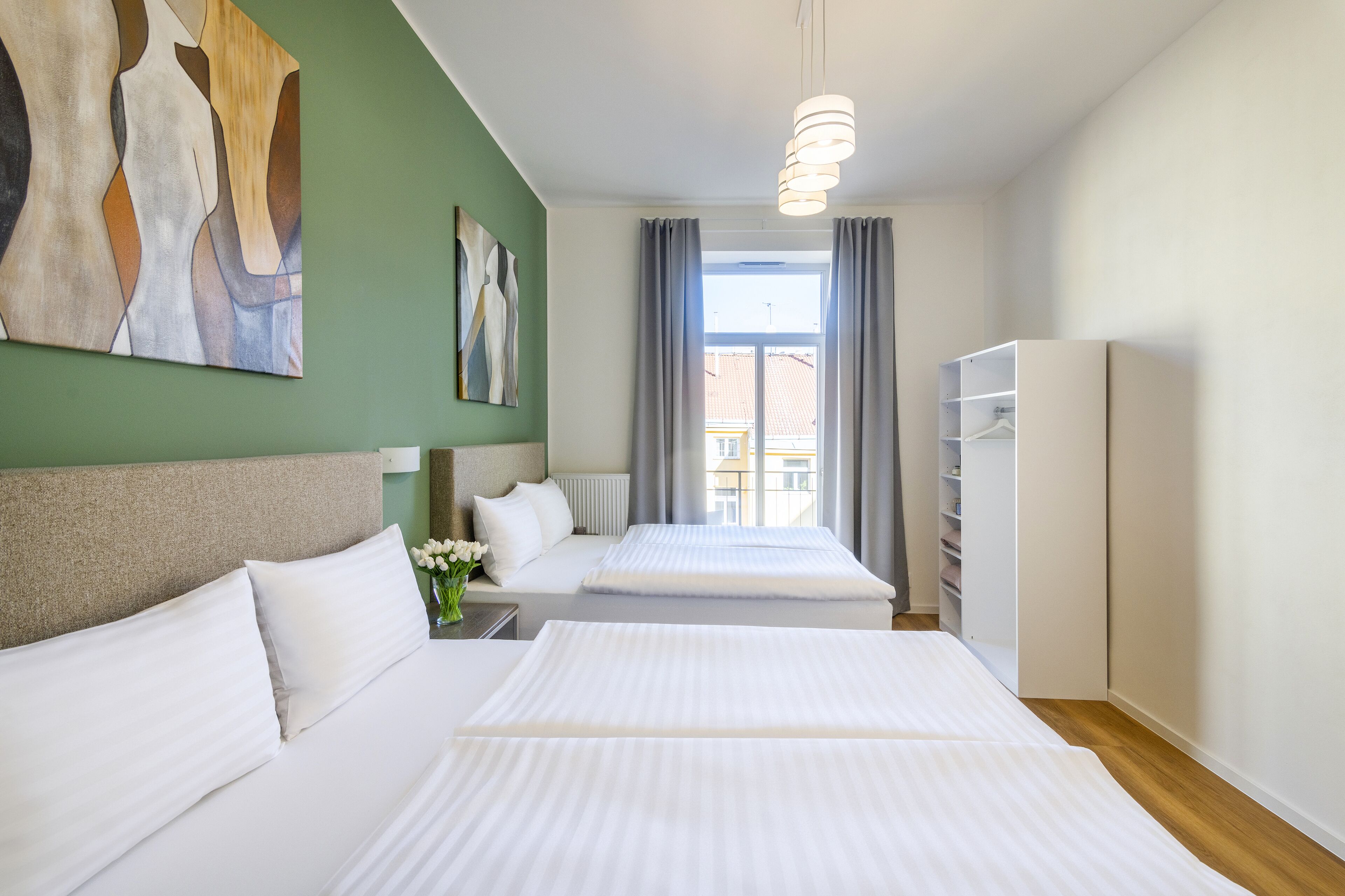 A hotel room with two beds, a large window, a wardrobe, and artwork on the walls.
