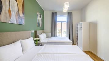A hotel room with two beds, a large window, a wardrobe, and artwork on the walls.