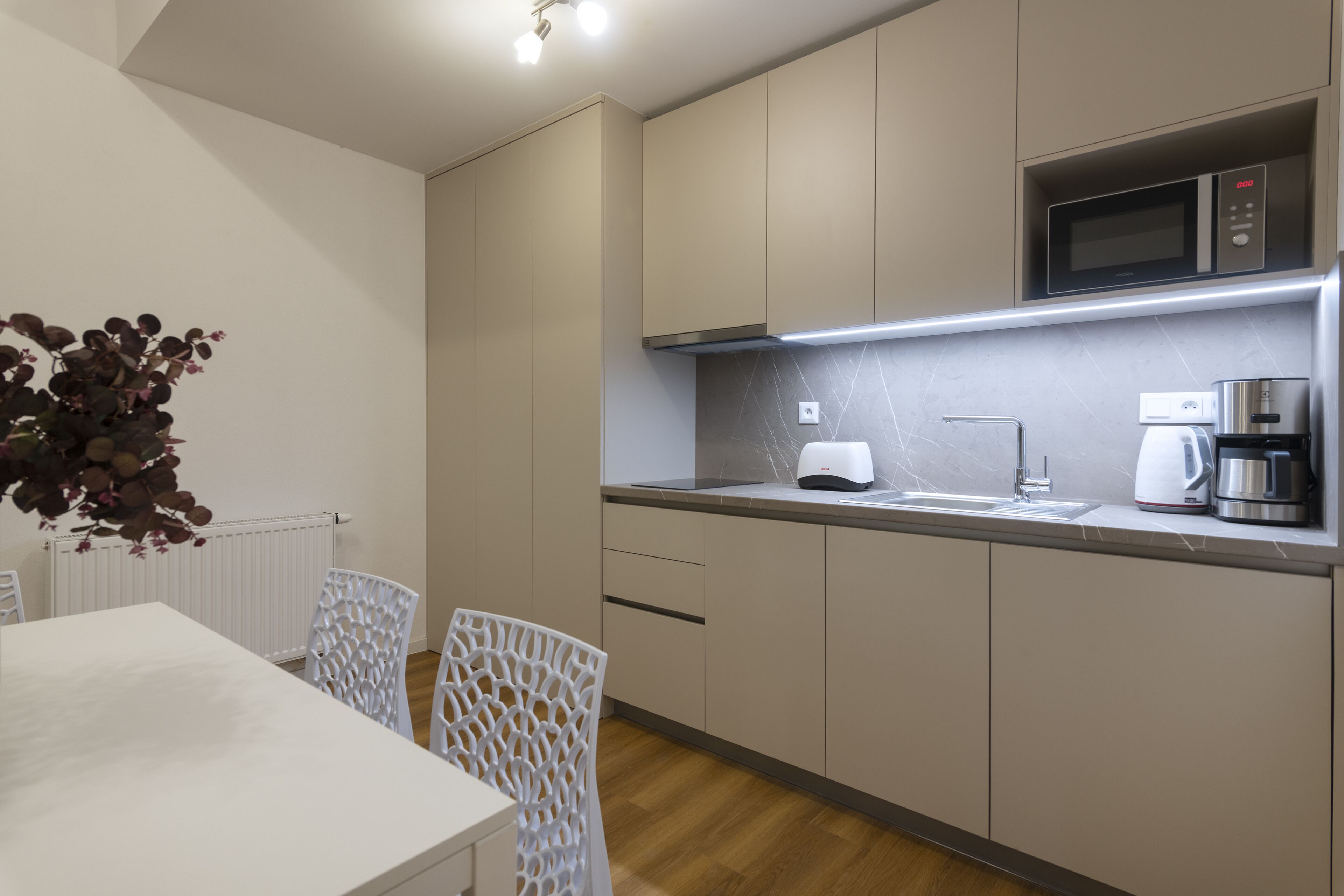 A modern kitchen with a microwave, coffee maker, and sink. There is a dining table with chairs.