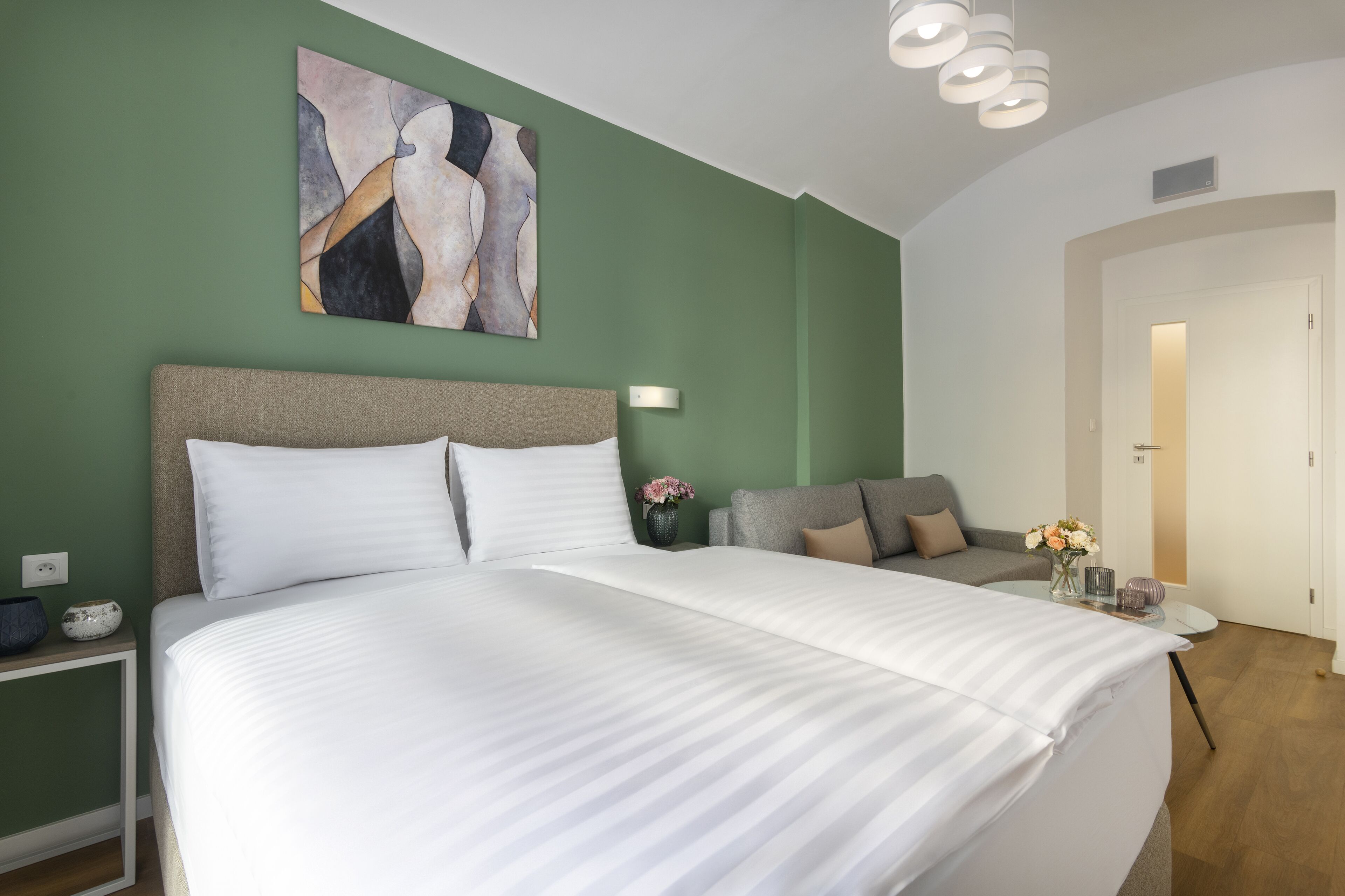 A modern hotel room with a large bed, a sofa, and a painting on the wall.