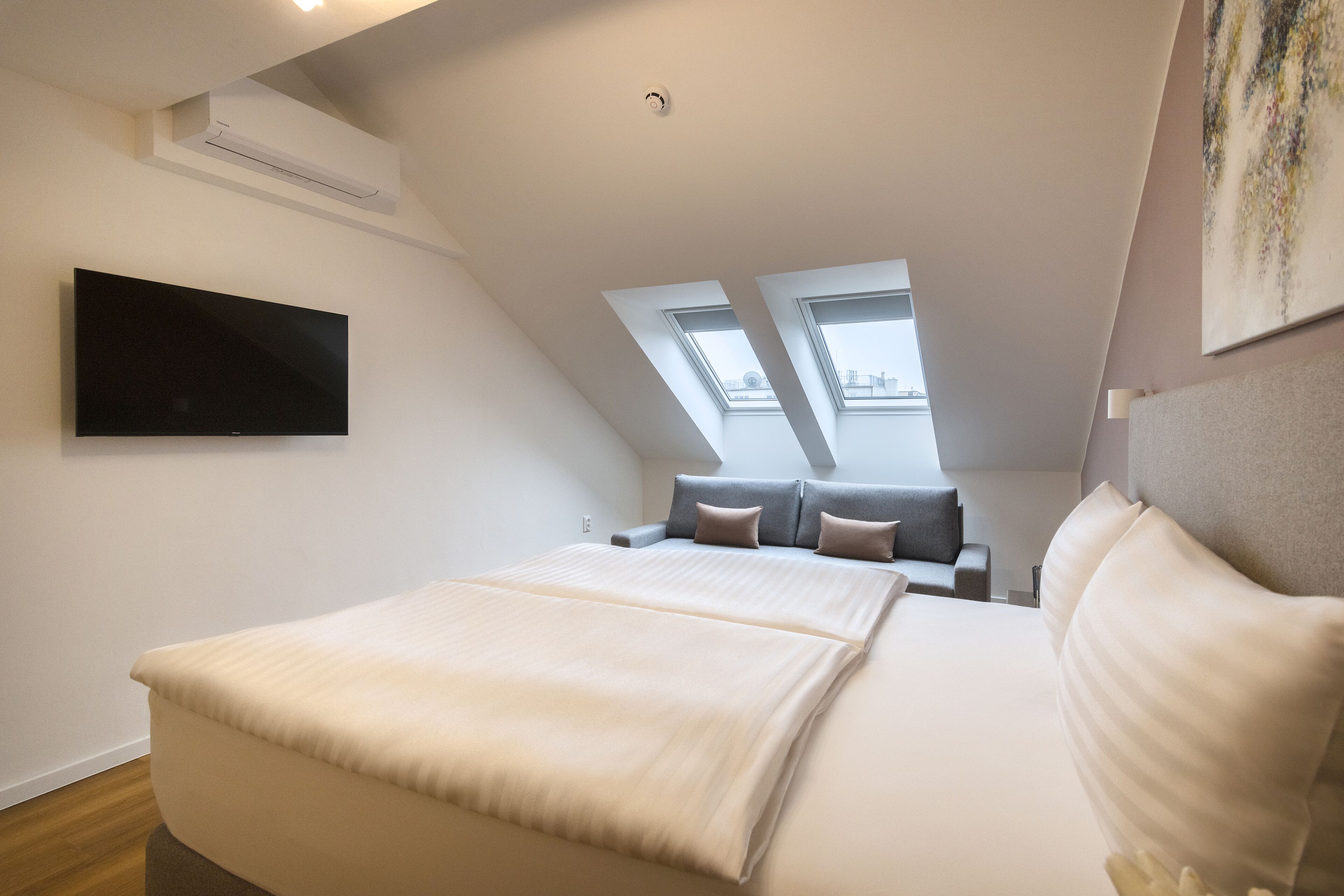 Un dormitorio moderno con una cama grande, un televisor de pantalla plana, un sofá y tragaluces.
