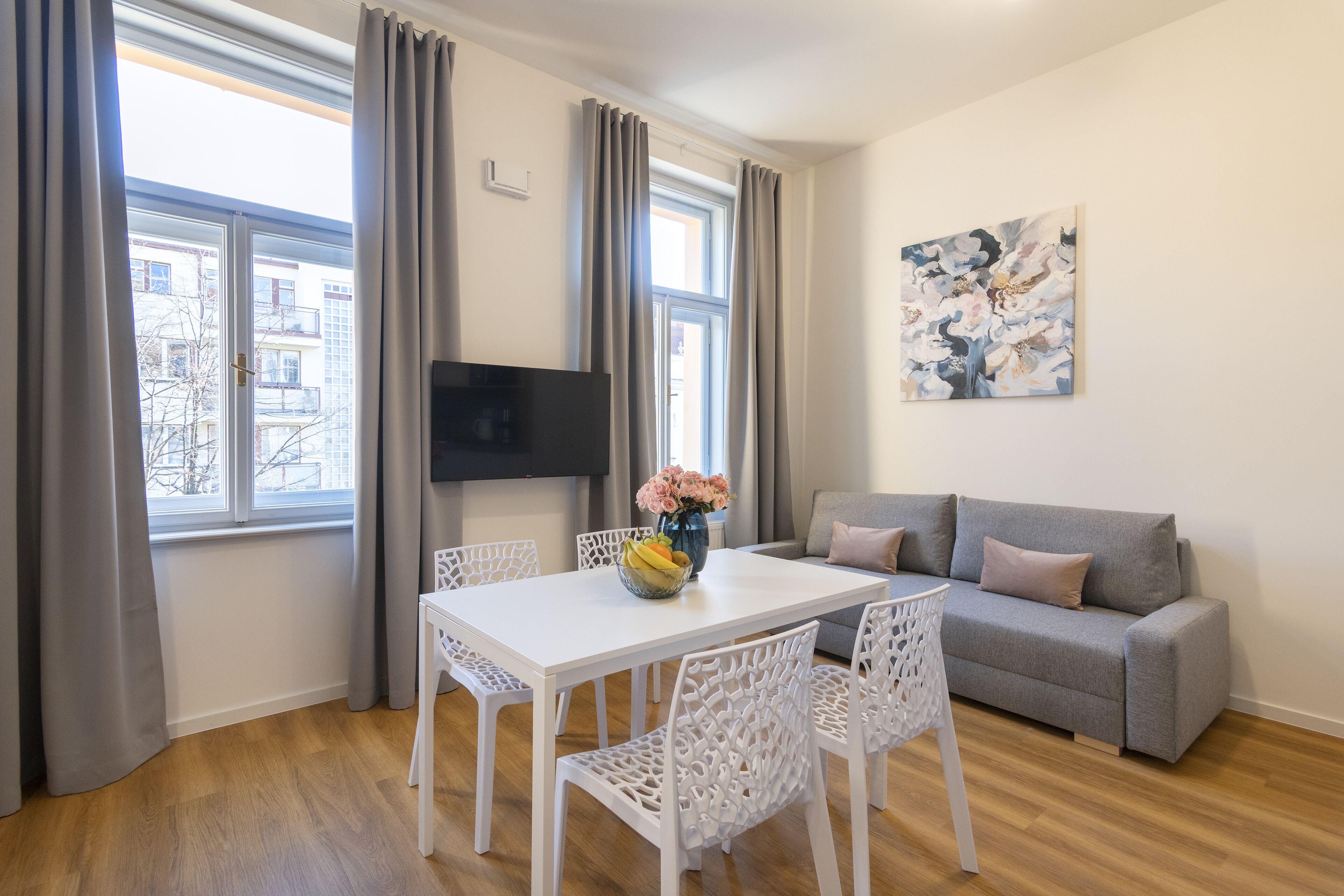 Ein modernes Wohnzimmer mit einem weißen Tisch und Stühlen, einem grauen Sofa und einem an der Wand befestigten Flachbildfernseher.