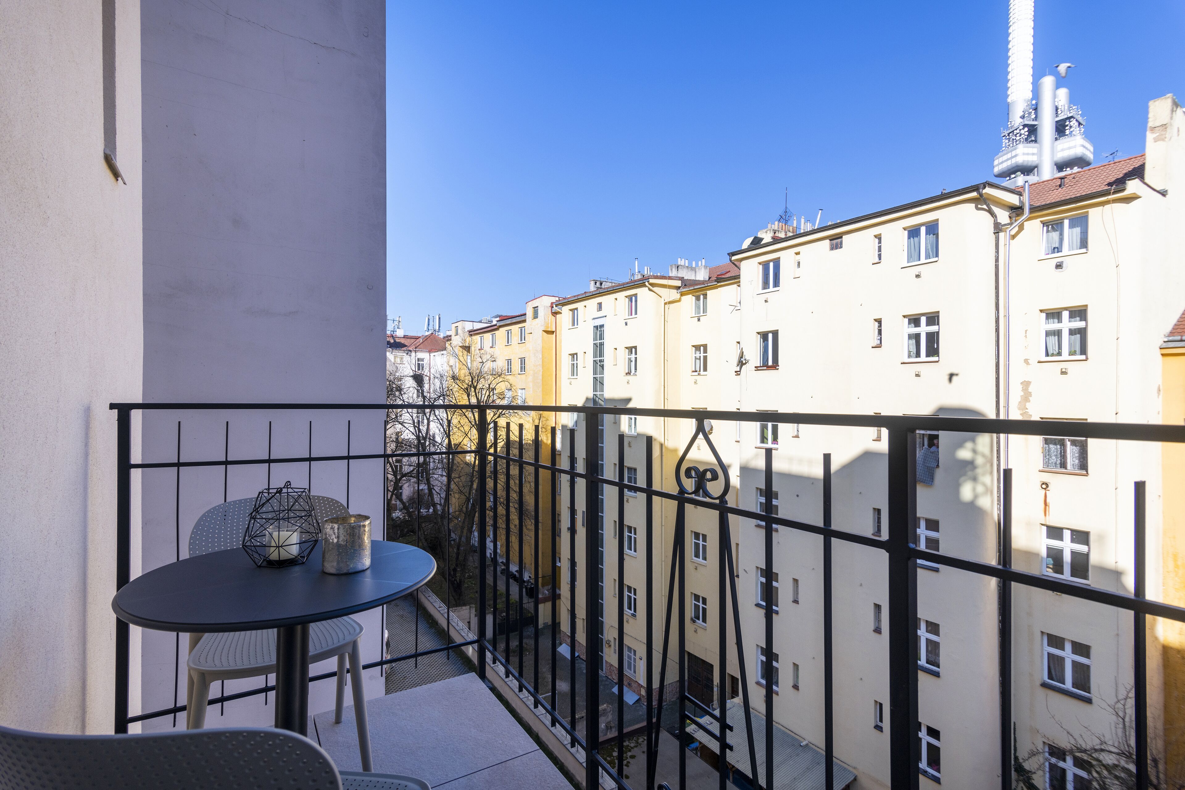 A balcony with a table and chairs, overlooking a row of buildings with multiple windows and balconies.