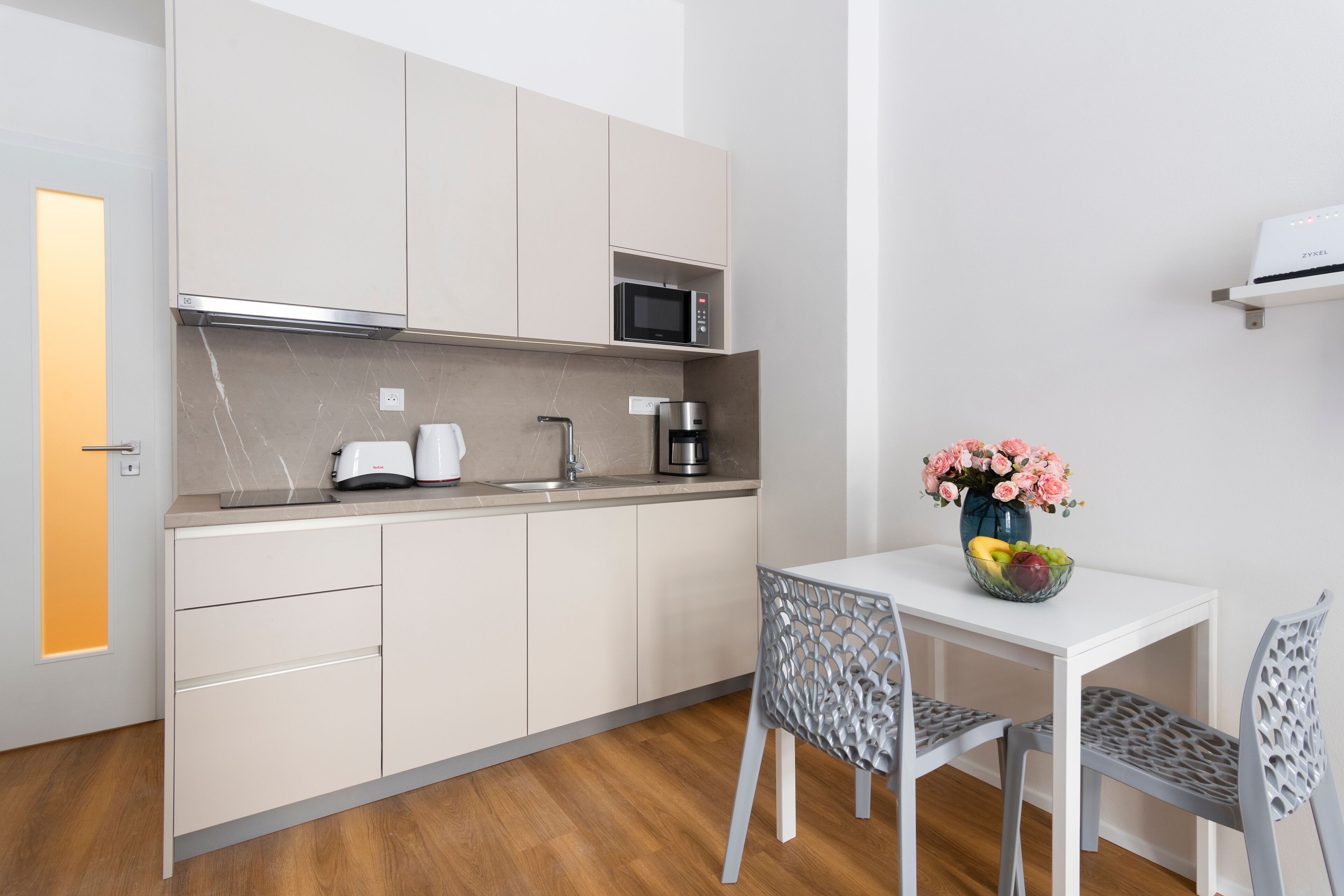 Una cucina moderna con forno a microonde, macchina del caffè e un vaso con fiori sul tavolo.