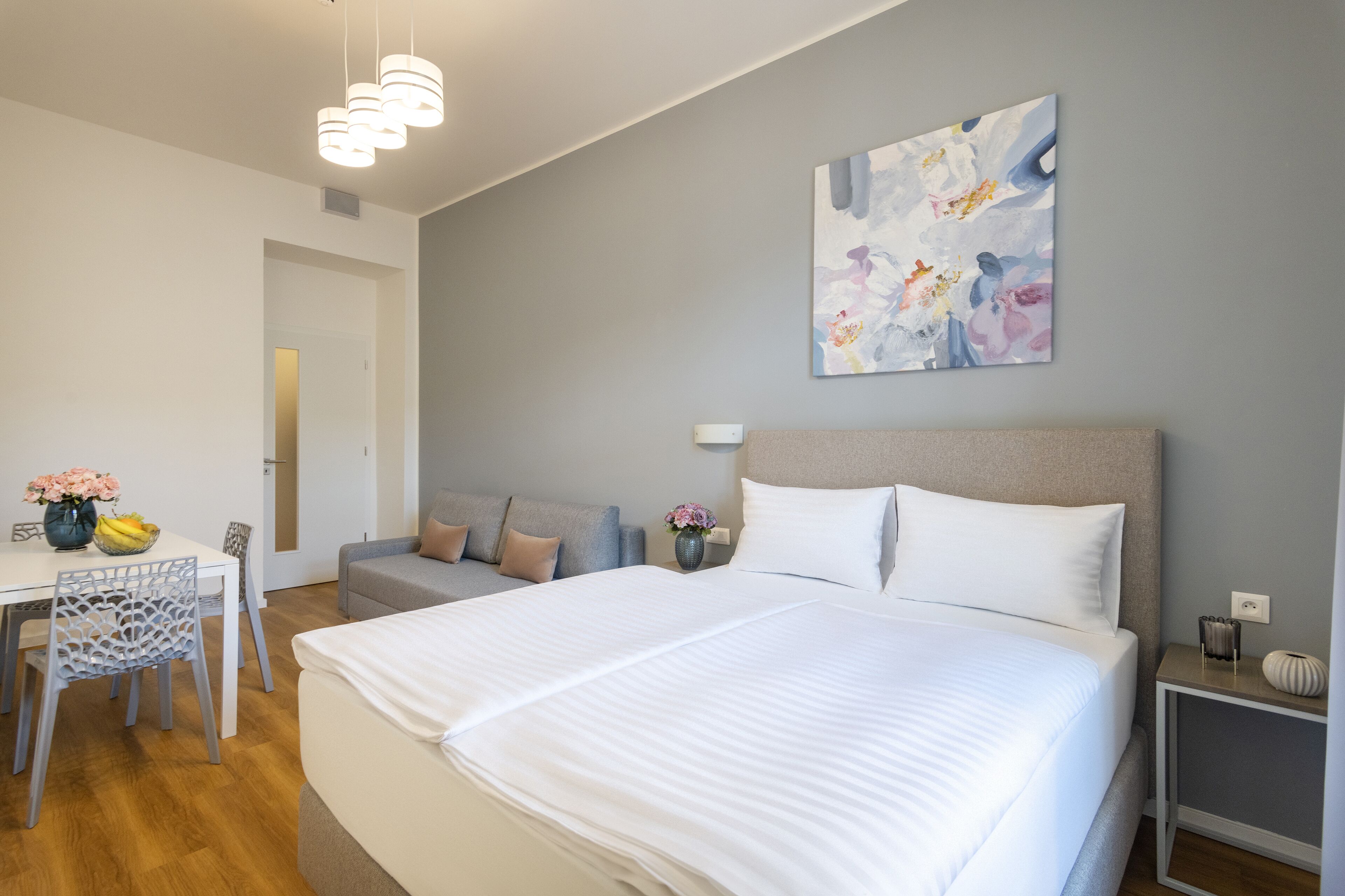 Una habitación de hotel moderna con una cama grande, un sofá, una mesa de comedor con sillas y un cuadro en la pared.