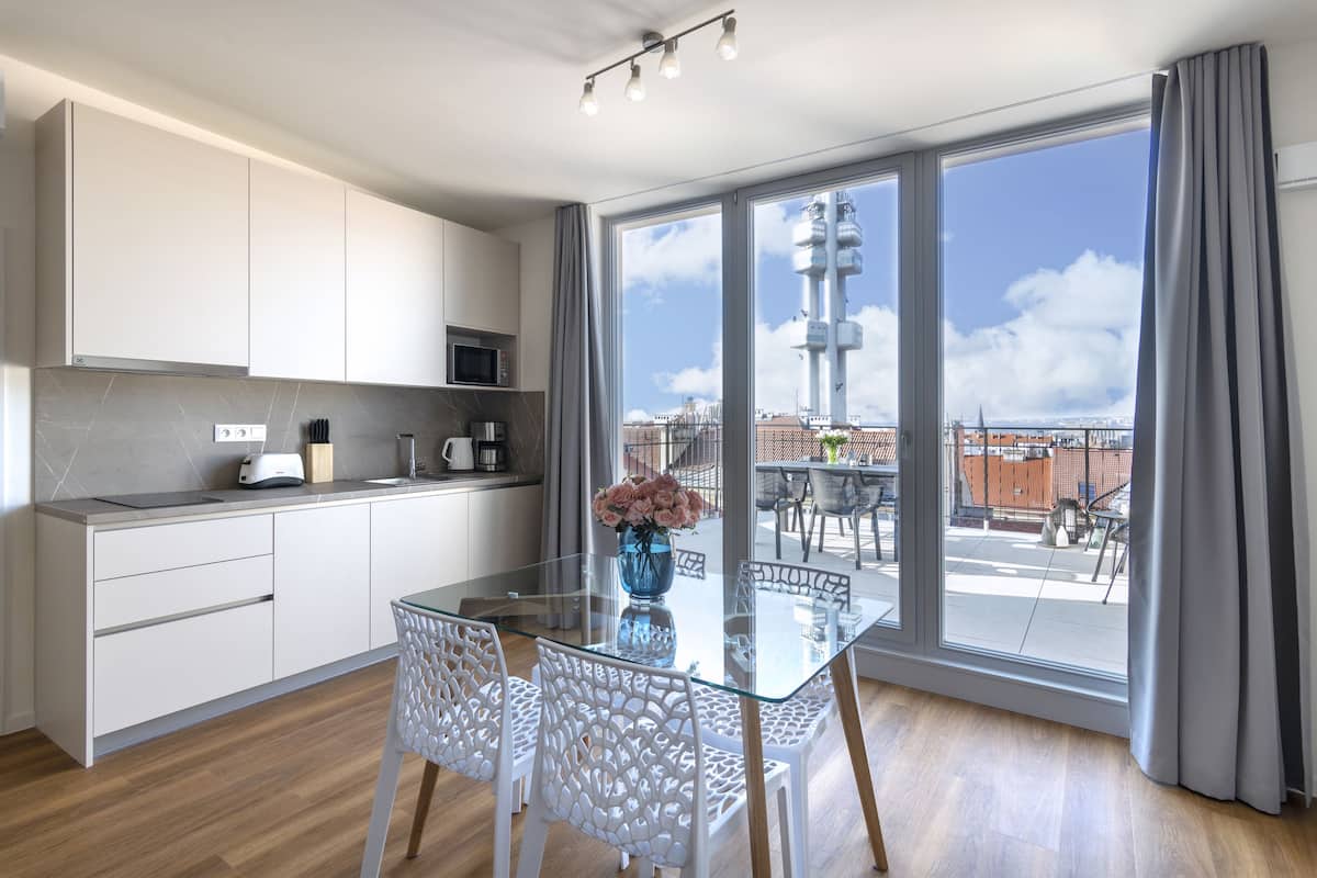 Una cocina moderna con armarios blancos, una mesa de comedor de vidrio y vistas de la ciudad a través de amplias ventanas.