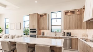 A modern kitchen with a large island, built-in ovens, and wooden cabinetry. - Naples Calming Waves Luxury Beach Home Heated Pool/Spa Walk 2 Beach (Naples)