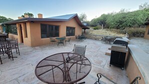 A patio area with a round metal table, several chairs, a barbecue grill, and a stone-tiled floor. - Boutique Hillside Hotel with Breathtaking Vistas. BBQ, Hiking Trail & Dark Skies (Oracle)