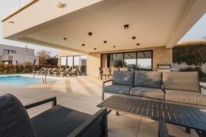 A modern outdoor patio with a pool, lounge chairs, a sofa, and a grill. - Luxury 4BD villa for 8 with pool, jacuzzi, sauna, gym, bocci and basketball (Brnobići)