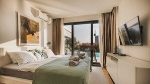 Une chambre d’hôtel moderne équipée d’un lit, d’un téléviseur à écran plat, d’un tableau et offrant une vue sur une piscine et un espace verdoyant.
