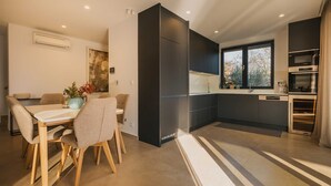 Une cuisine moderne avec des meubles de couleur sombre, un coin repas comprenant une table et des chaises, et une grande fenêtre laissant entrer la lumière naturelle.