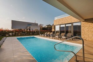 A modern outdoor pool area with lounge chairs and a clear blue pool. - Luxury 4BD villa for 8 with pool, jacuzzi, sauna, gym, bocci and basketball (Brnobići)